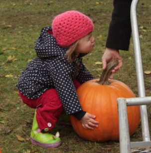Picture of a small child trying to pick up a large pumpkin